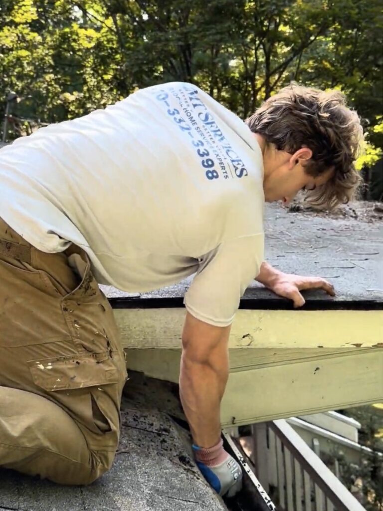 2MT Services crew member in a branded shirt clearing debris from a gutter by hand