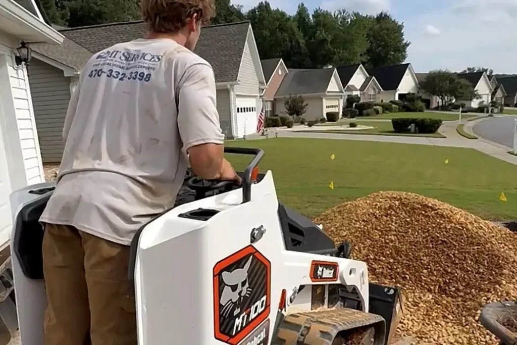 2MT Services crew member in a branded shirt operating a Bobcat track loader on a driveway job in Kennesaw, Georgia