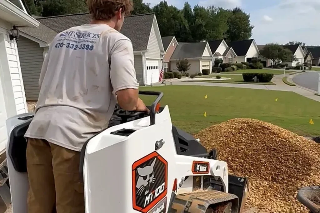 2MT Services crew member in a branded shirt operating a Bobcat track loader on a driveway job in Kennesaw, Georgia