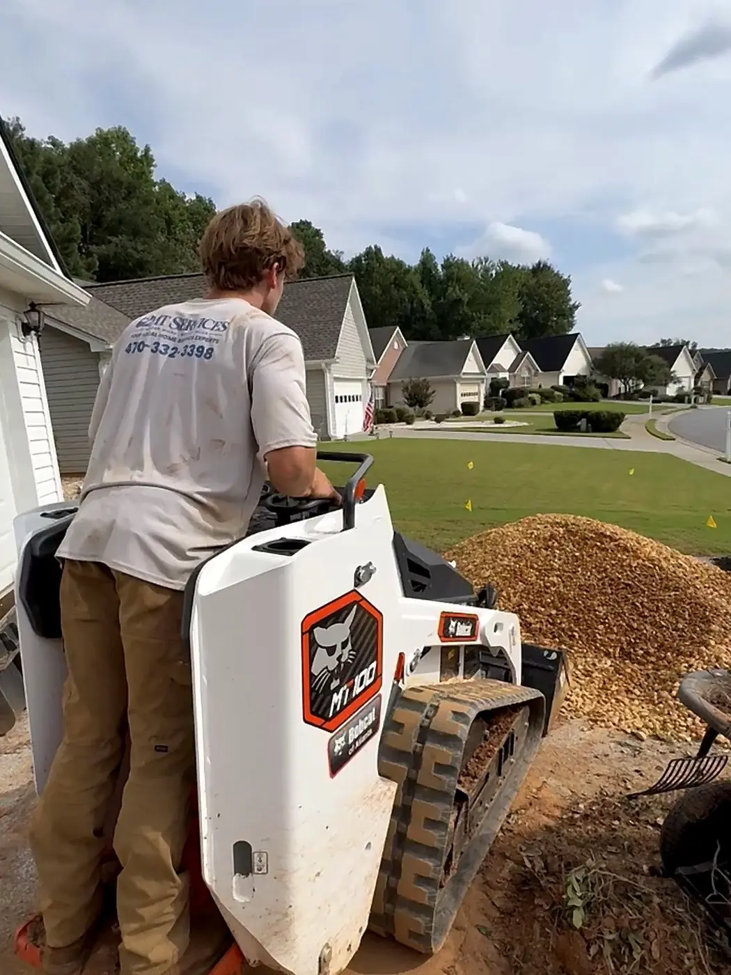 2MT Services crew member in a branded shirt operating a Bobcat track loader on a driveway job in Kennesaw, Georgia
