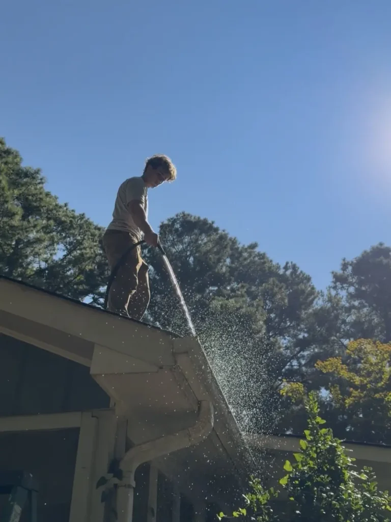 Flushing a gutter with a hose after cleaning to check that the downspouts run clear