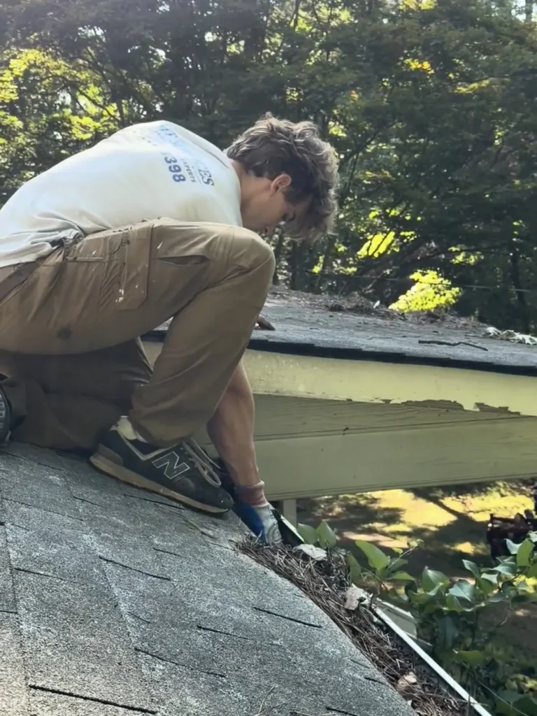 Mason of 2MT Services hand-cleaning a gutter packed with pine needles on a Kennesaw, Georgia roof